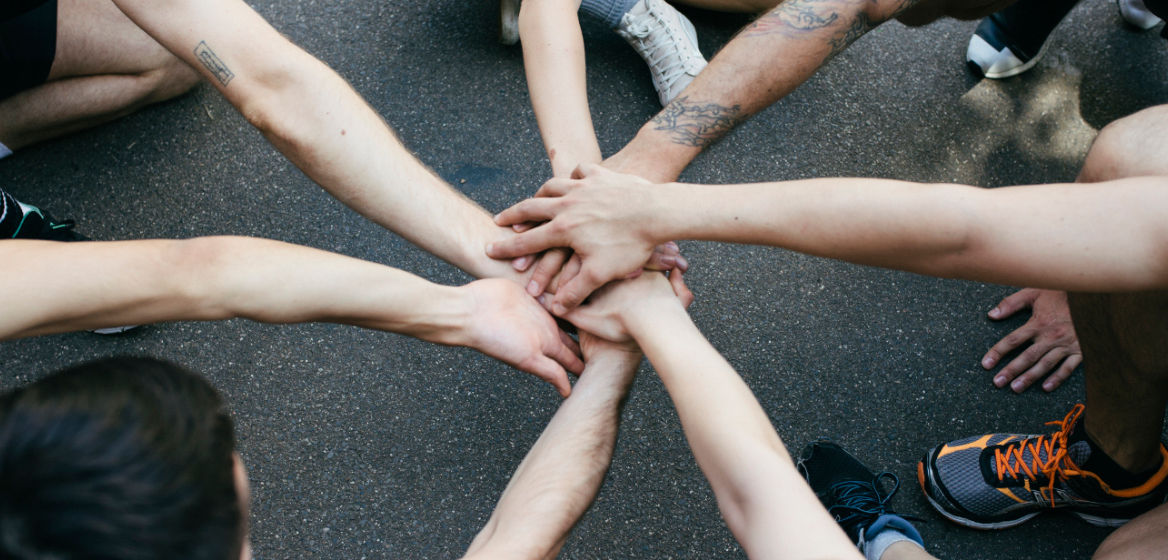 A group of amateur athletes bring their hands together in a show of unity and sportsmanship before playing a friendly game of basketball outdoors.