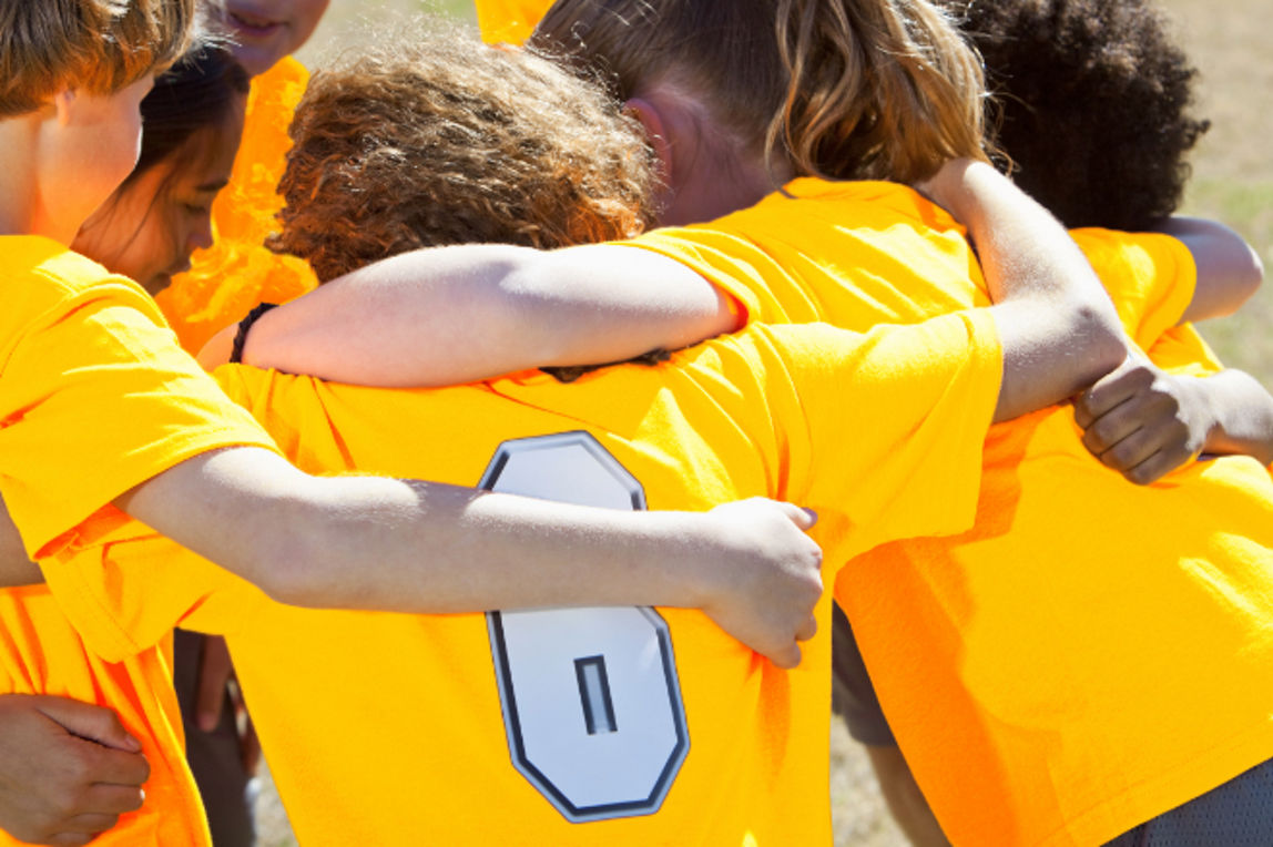 Kinder in Sporttrikots bilden einen Kreis mit um die Schultern gelegten Armen