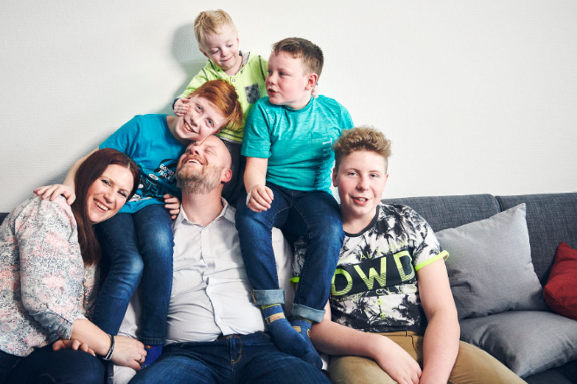 Familie mit vier Söhnen posiert vergnügt auf dem Sofa
