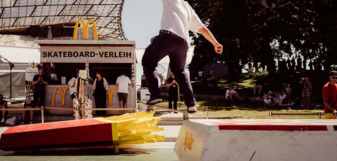 Skateboardfahrer in Skatepark mit Hindernissen in Form von McDonald's Produkten