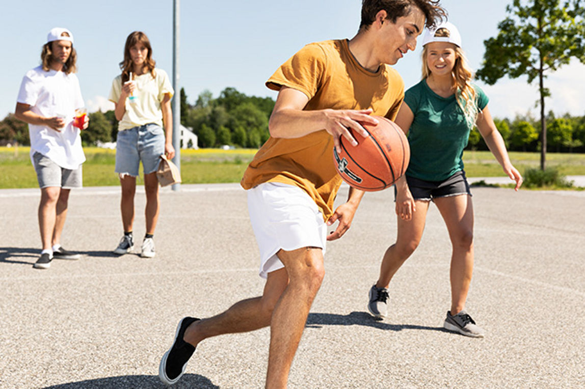 Jugendliche spielen auf einem Steinplatz Basketball
