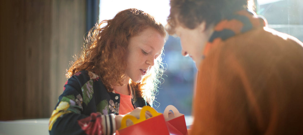 A girl eating a happy meal with an adult in the foreground