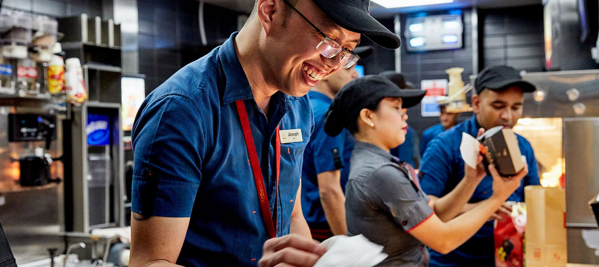 A McDonald's employee smiling in the foreground with other employees working in the background