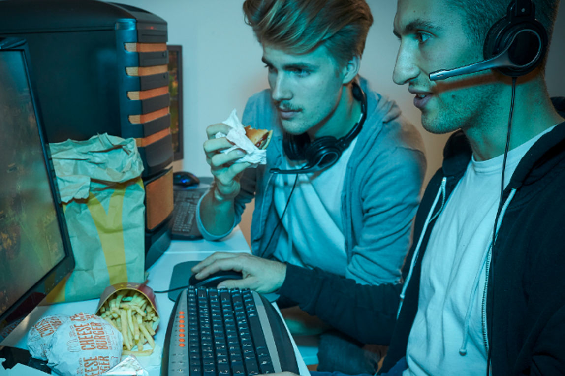Zwei Gamer schauen gebannt auf einen Computer-Bildschirm und essen dabei McDonald's-Produkte