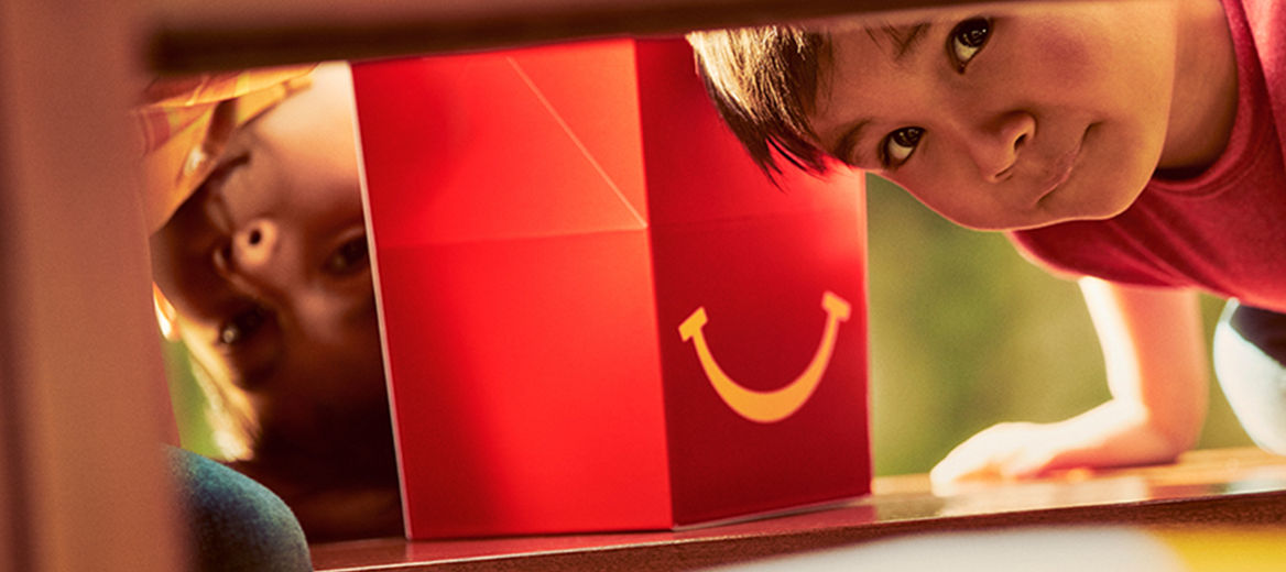 Young girl holding red Happy Meal box close to her face and looking through the yellow handle