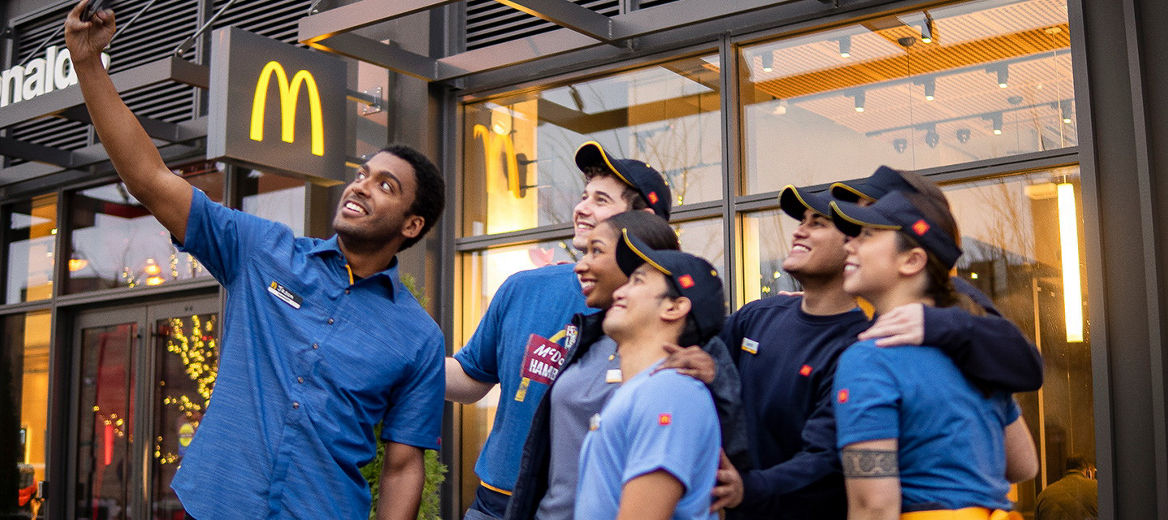Seven McDonald's employees standing together outside a restaurant taking a photo