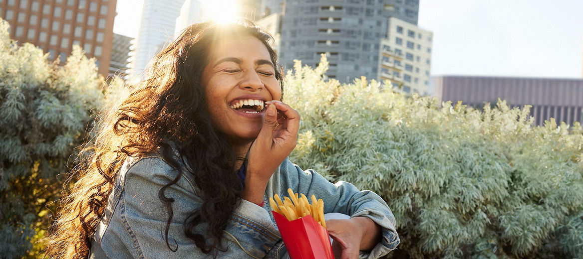 A woman smiling in the sun holding fries