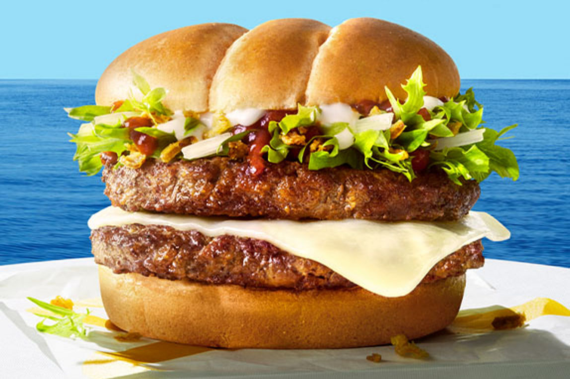 A delicious looking Beef burger on a white tablecloth in front of a seascape background.