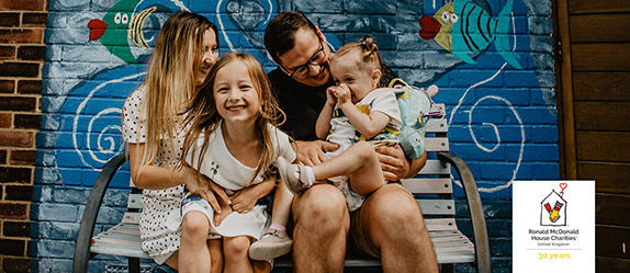 Family sitting on a bench in front of a mural. 