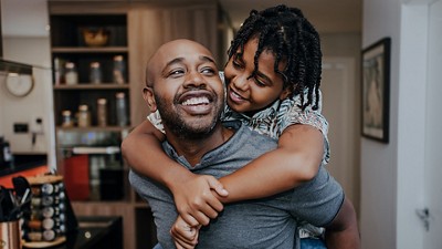 A daughter hugs her dad, smiling, from behind