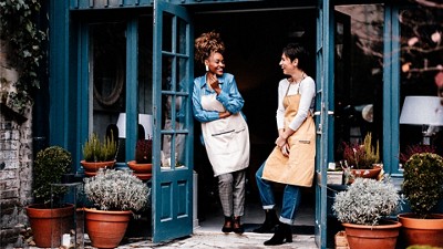 Two smiling women standing in the doorway of a business talking