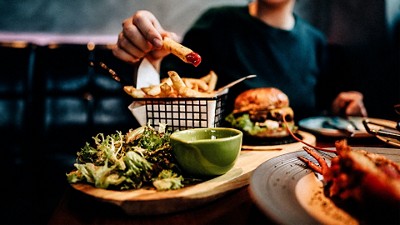 Person dipping a fry in ketchup and a juicy burger is featured in the background