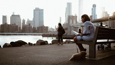 Woman sitting on a bench reading a book in front of a city skyline 