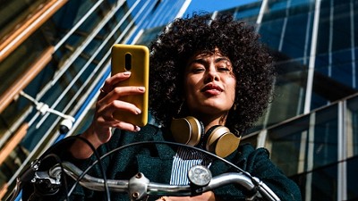 Curly haired woman posing for a picture holding a phone and sitting and a bike