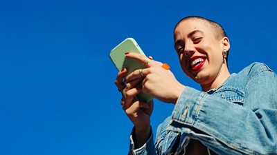 Woman holding a phone and smiling with a blue sky behind her