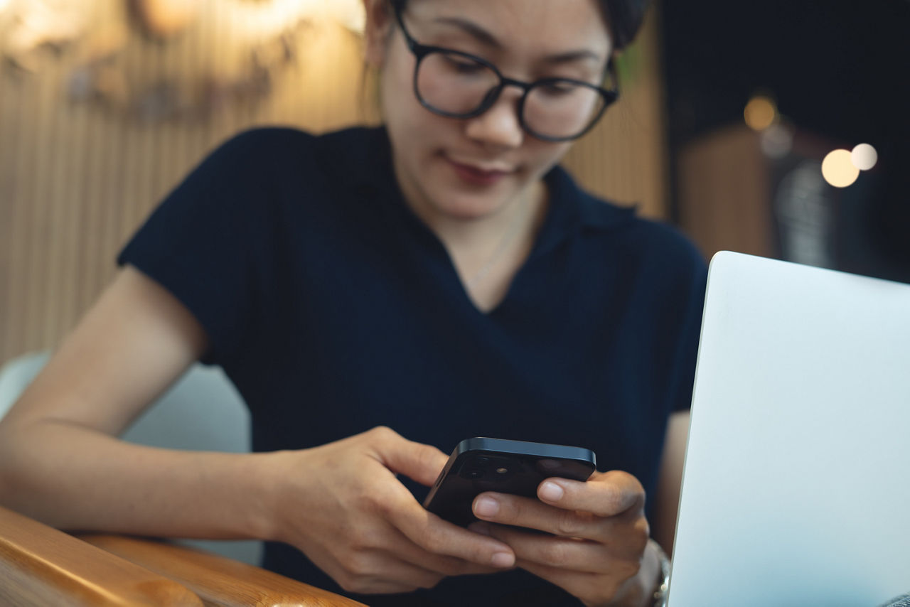 Young asian woman using mobile phone and laptop computer remote working at coffee shop. Woman using smartphone for online shopping and internet banking via mobile app, social media networking