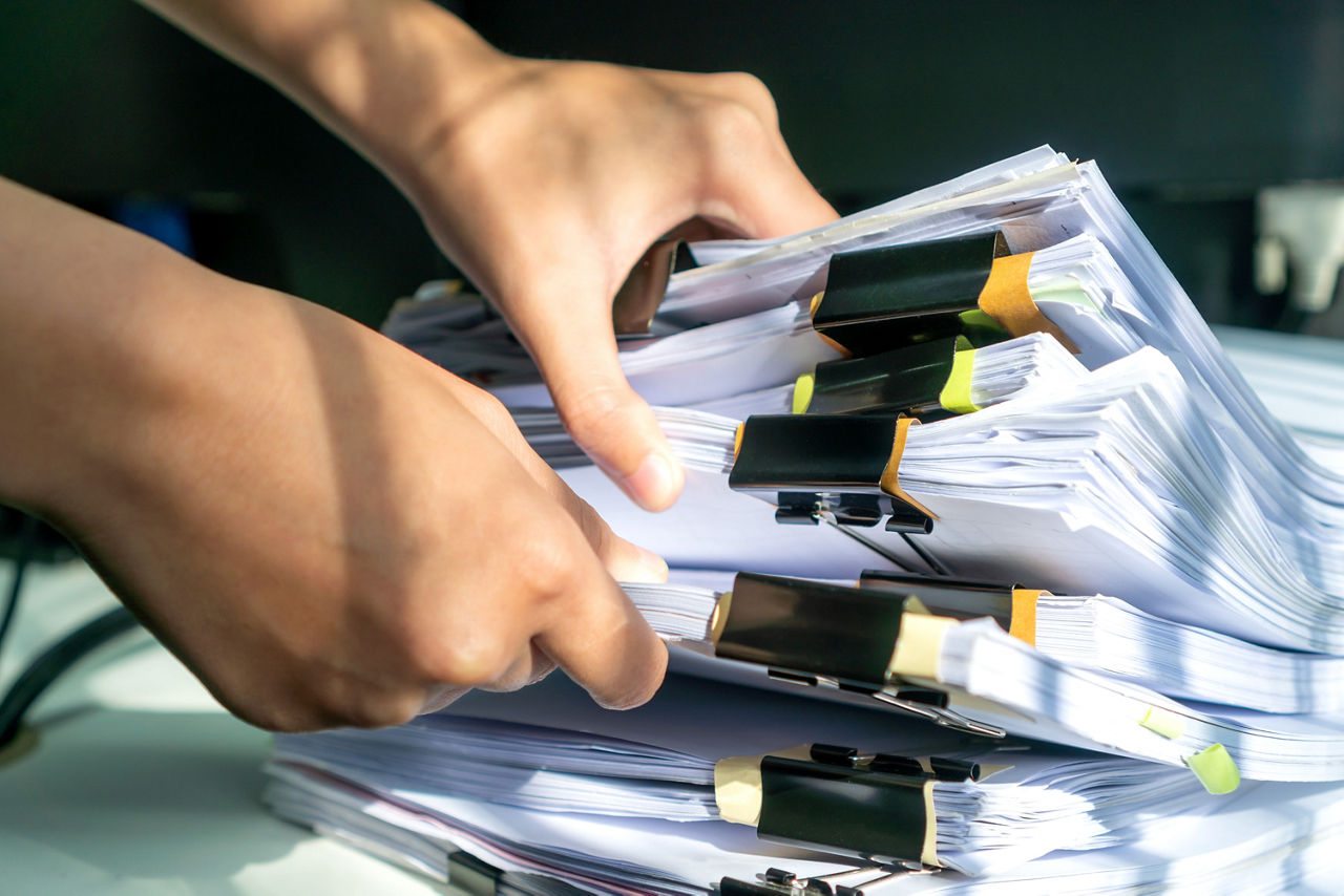 Businesswoman working in stacks of paperwork files for searching infomation unfinished documents about pile audit form on desk office and investigate financial doc in busy workload