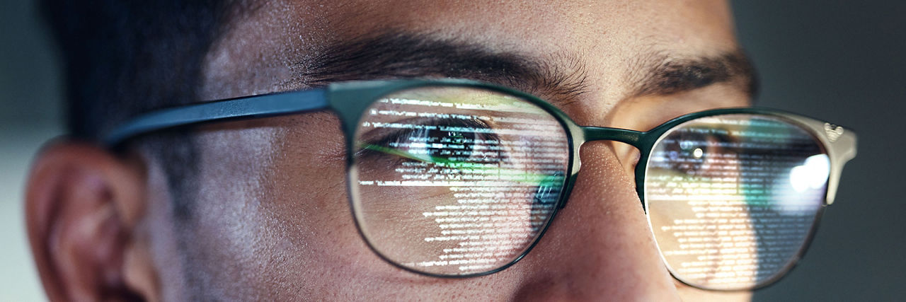 Glasses, man and reflection of programmer on computer working on software, code and data. IT, engineer and serious face of developer with information technology for cloud computing in office closeup.