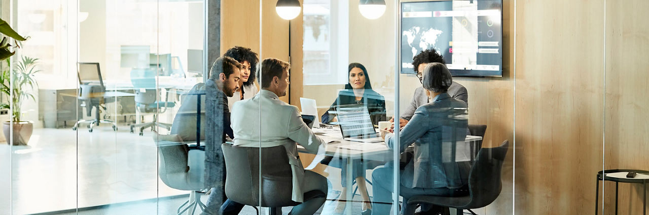 Business colleagues sitting at conference table seen through glass wall. Multi-ethnic coworkers are discussing in board room at office. They are planning strategy.