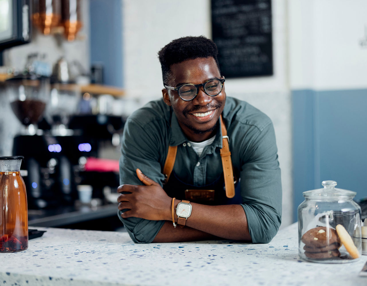 Cheerful African-American barista smiling and standing behind the counter of a cafeteria