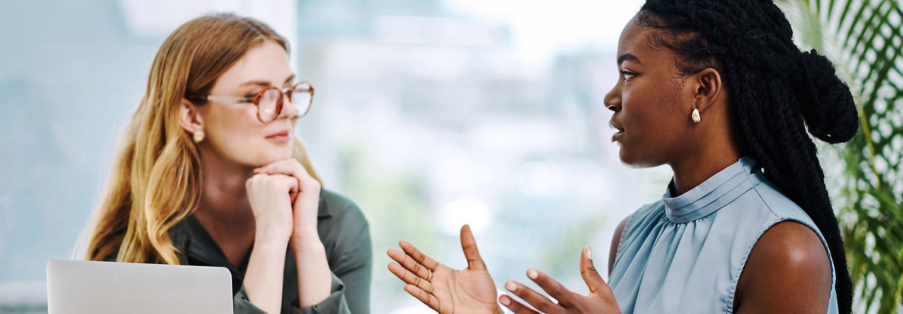 Two diverse businesswomen having a discussion to share ideas and plans while working together in an office
