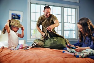 Military father packing duffle bag while daughters 