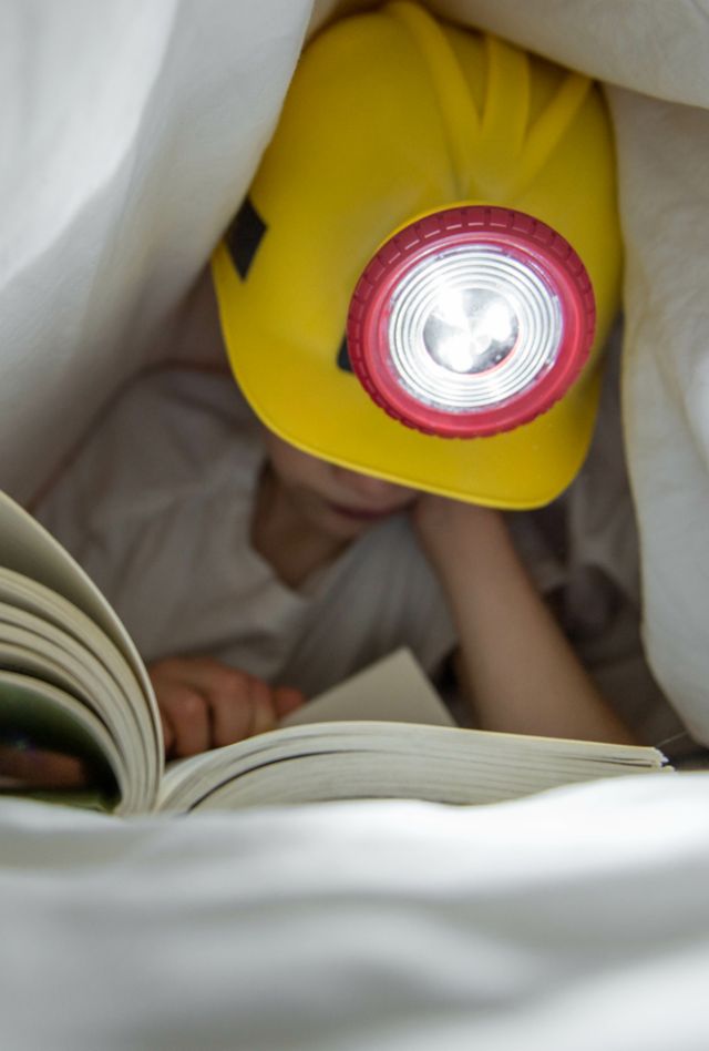 Child reads under the covers using a flashlight.