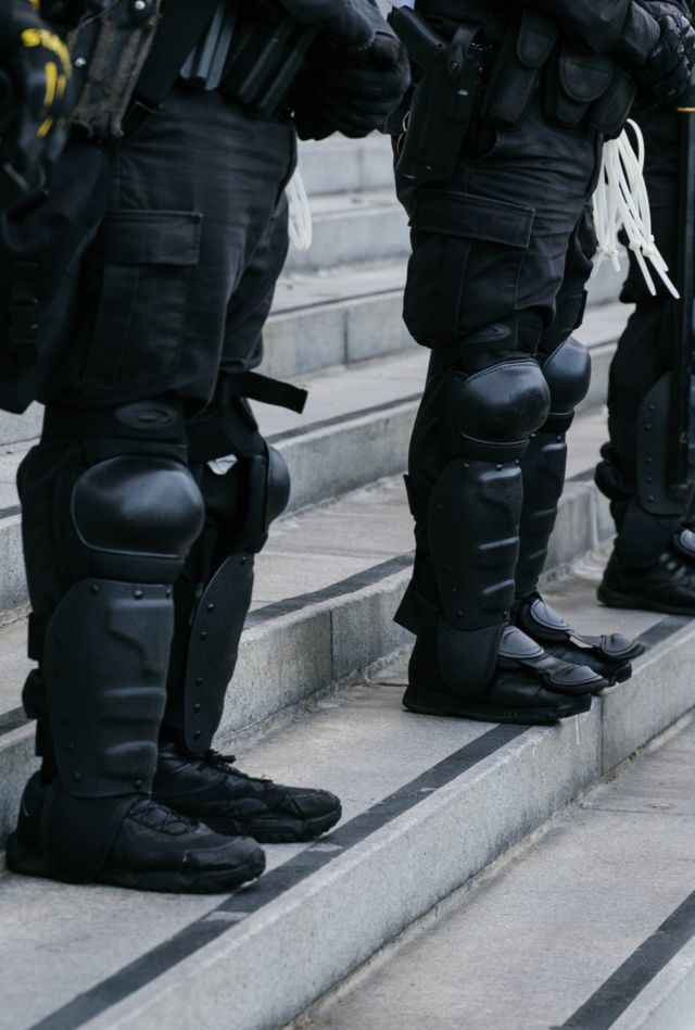 a line of police offices in combat suits behind barricades 