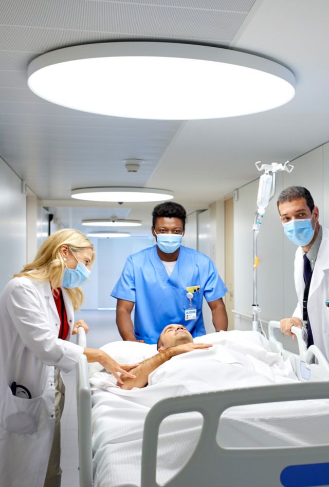 Medical professionals wearing  masks assisting a patient lying down in hospital bed