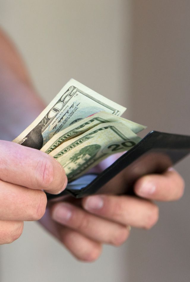 A close up of a man putting money in his wallet.