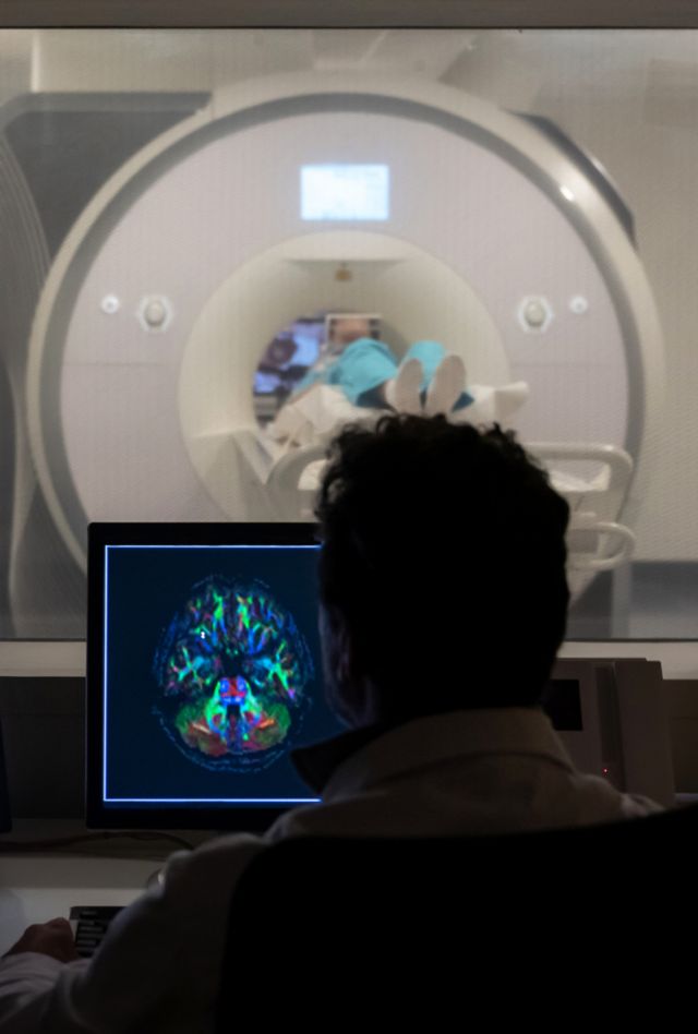 Back view of unrecognizable doctor in white robe sitting at table and analyzing MRI scan during procedure looking at a scan of a brain