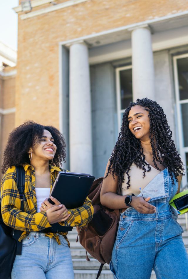 Happy female classmates wearing casual clothes leaving college. They are walking down the stairs of the faculty building while talking nonchalantly