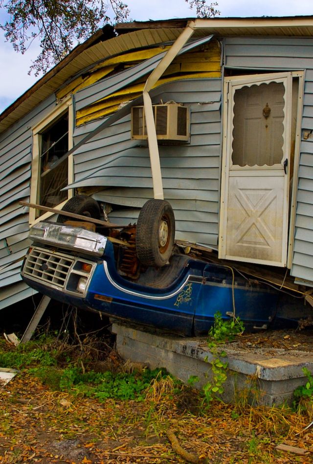 A building which appears to have been damaged by extreme weather sits on top of an upturned car