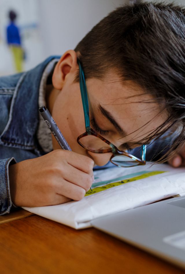 Pre-teen making a book gift for his dad and drawing and writing in Spanish over white paper and masking tape "para papa"