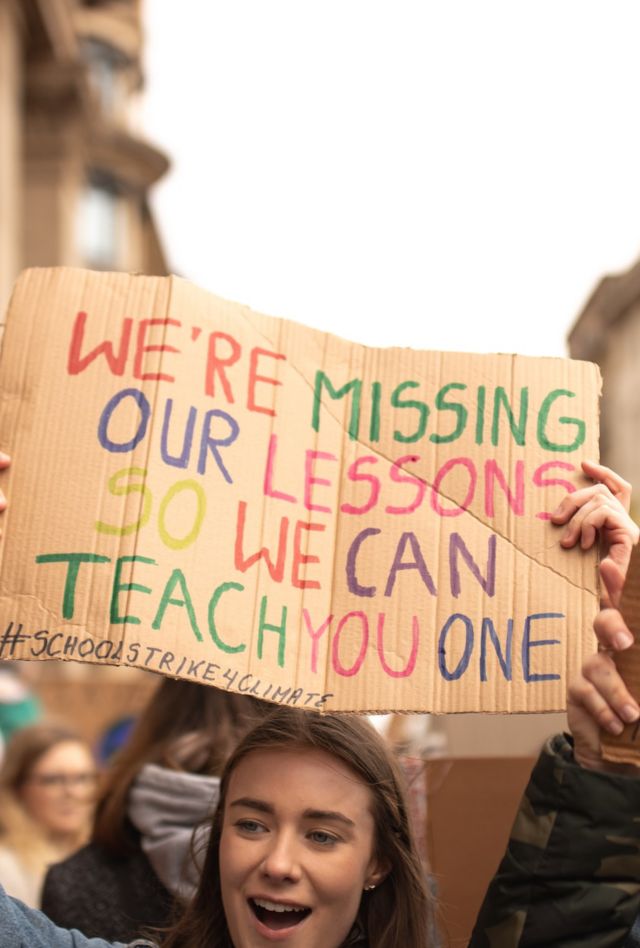 A crowd of people holds signs, one reading: We're Missing our lessons so we can teach you one #SchoolStrike4Climate