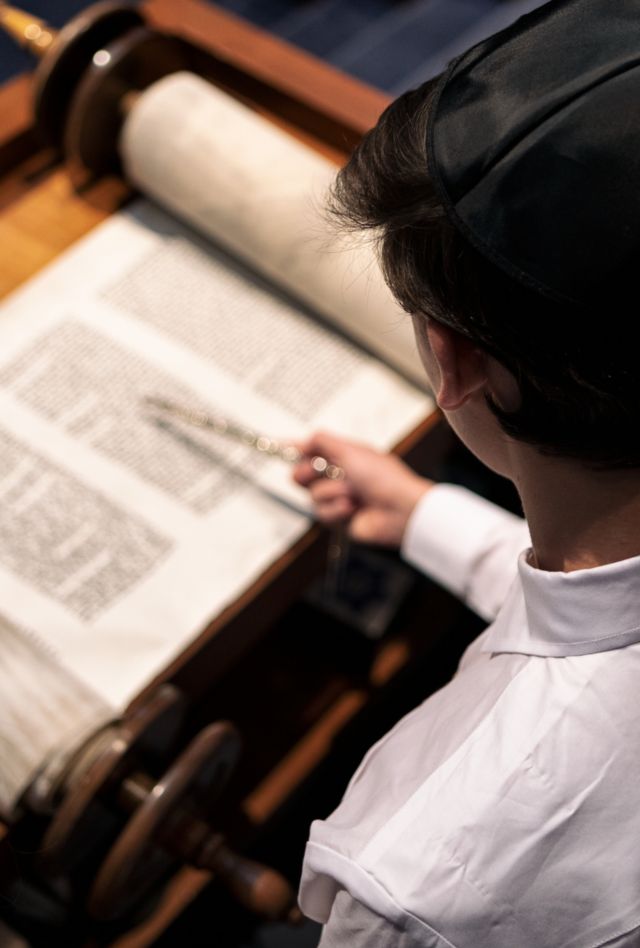 Overhead view of an adolescent boy and two adults reading the Torah