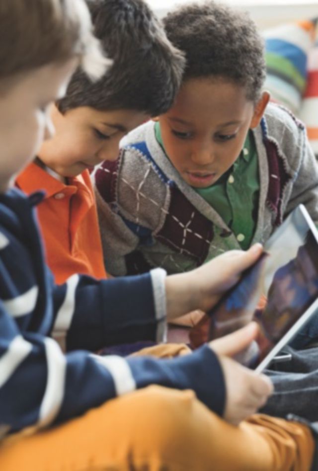 A group of children sitting in a classroom look at a tablet