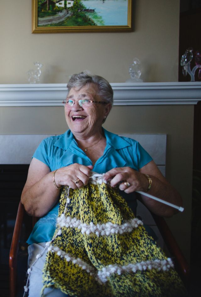 Two women sit next to each other laughing while knitting