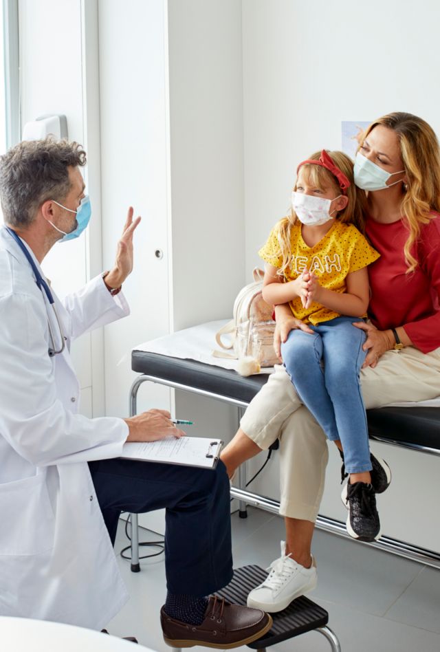 Pediatrician talking to to his patient accompanied by her mother all wearing masks