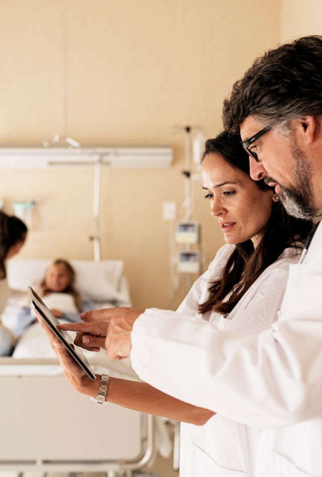 Medical staff evaluating tests in a tablet while patient and her mother are talking at background