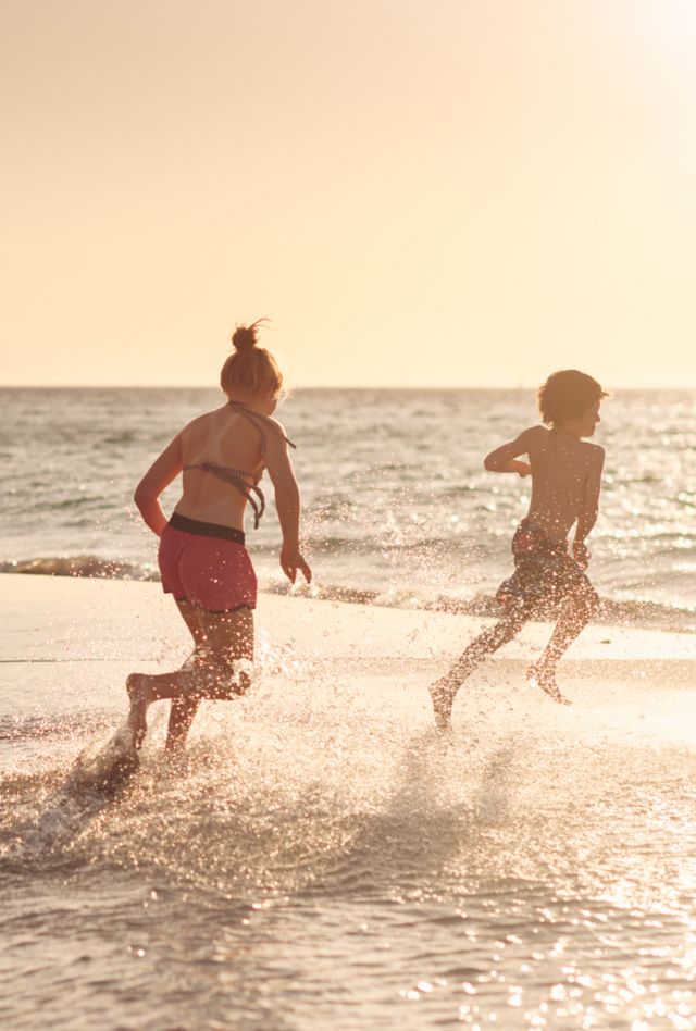 Two children play in the water on a beach at sunset