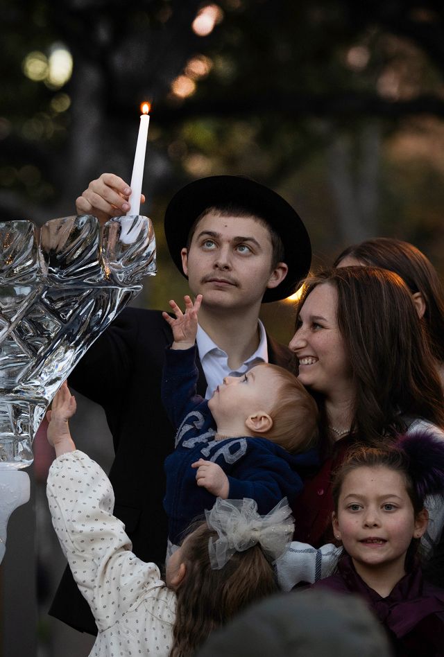 A man lights the first candle in a large menorah with his family