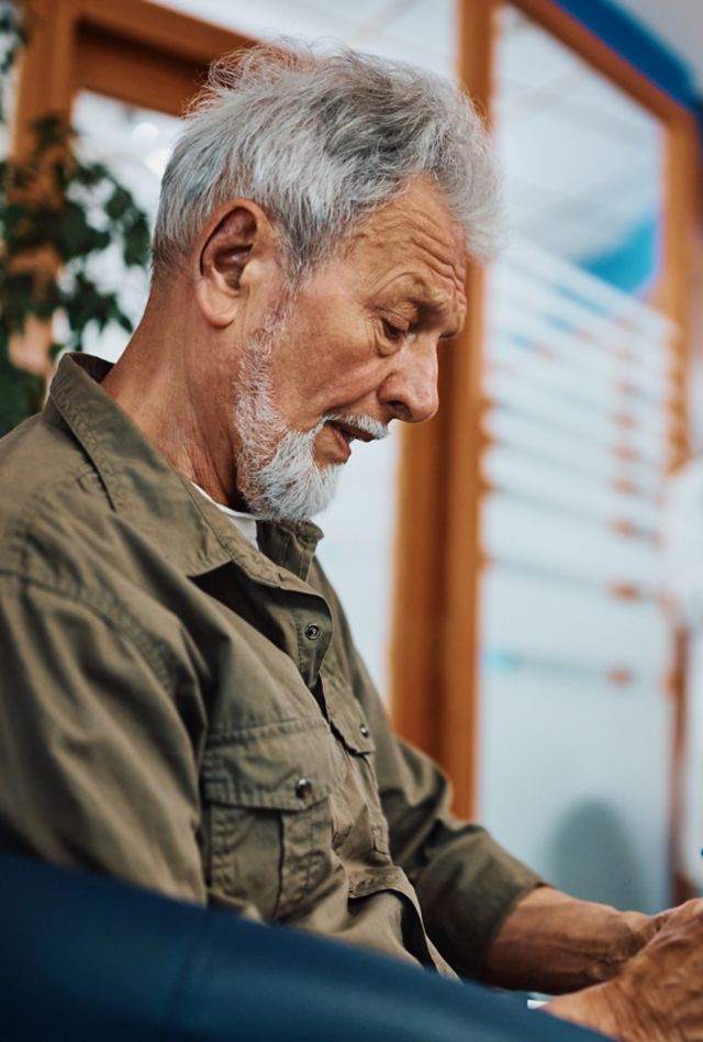 Older man filling out medical paperwork while sitting in waiting room at doctor's office