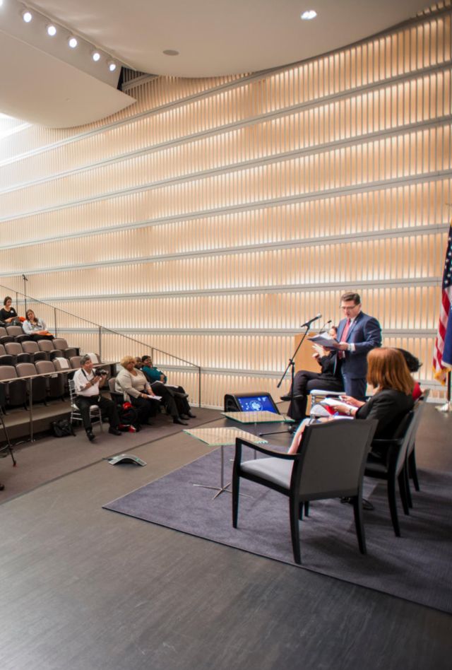 A man in a suit speaks to a large room of professionals