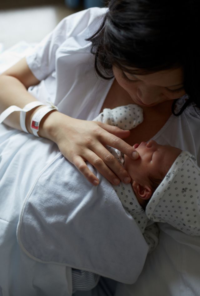 A woman holding a baby lies in a hospital bed