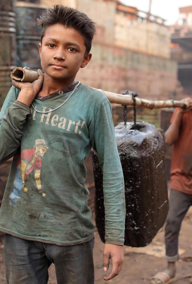 Two children carry a jug between them in a muddy street