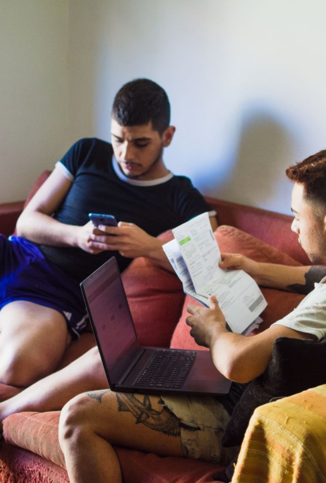 Young gay latino couple hanging out in the couch while they work on their home and personal finance with a laptop computer.