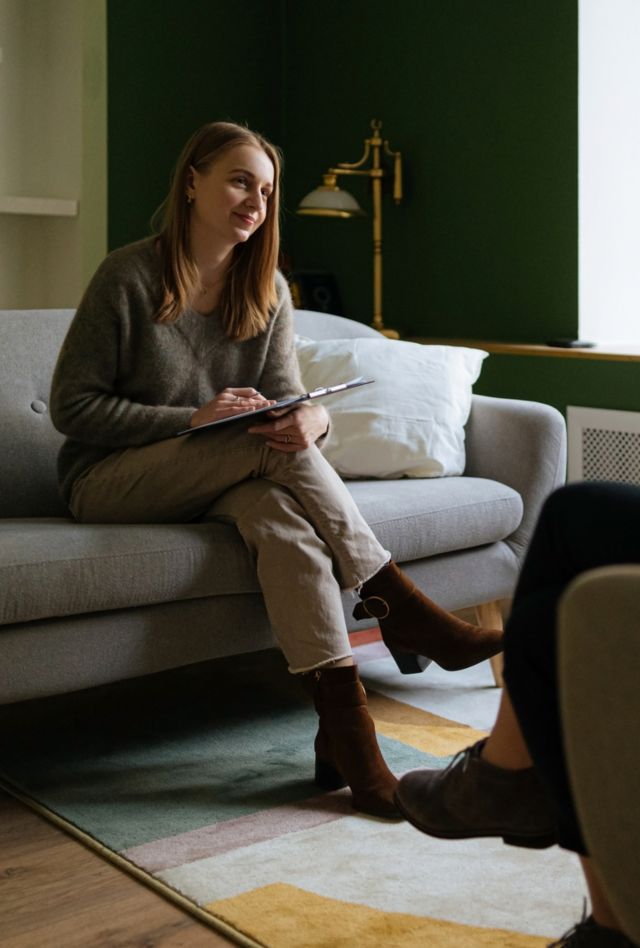 a benevolent young woman psychologist with a clipboard in her hands listens attentively to her client a woman during a therapy session in a beautiful and cozy office for a reception