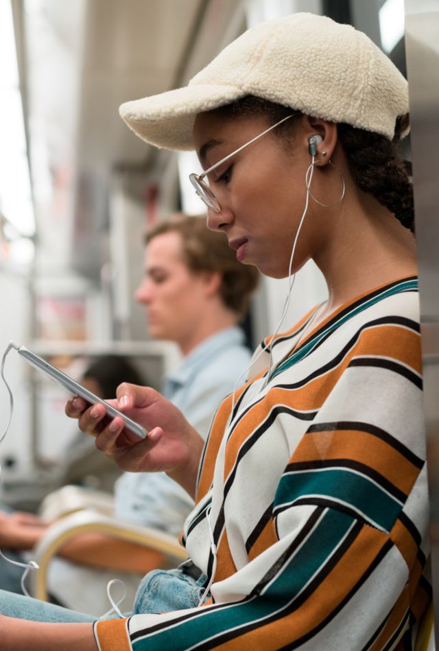 A person listening to music with earphones and looking at their phone while traveling on the subway.