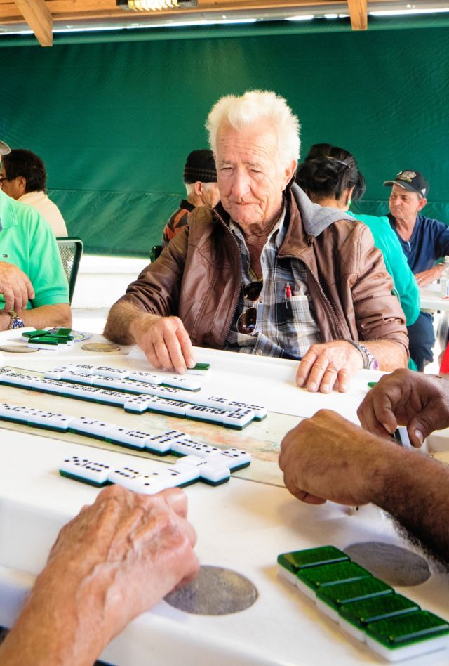 Mixed race senior men playing dominoes in Miami Little Havana at sidewalk tables.